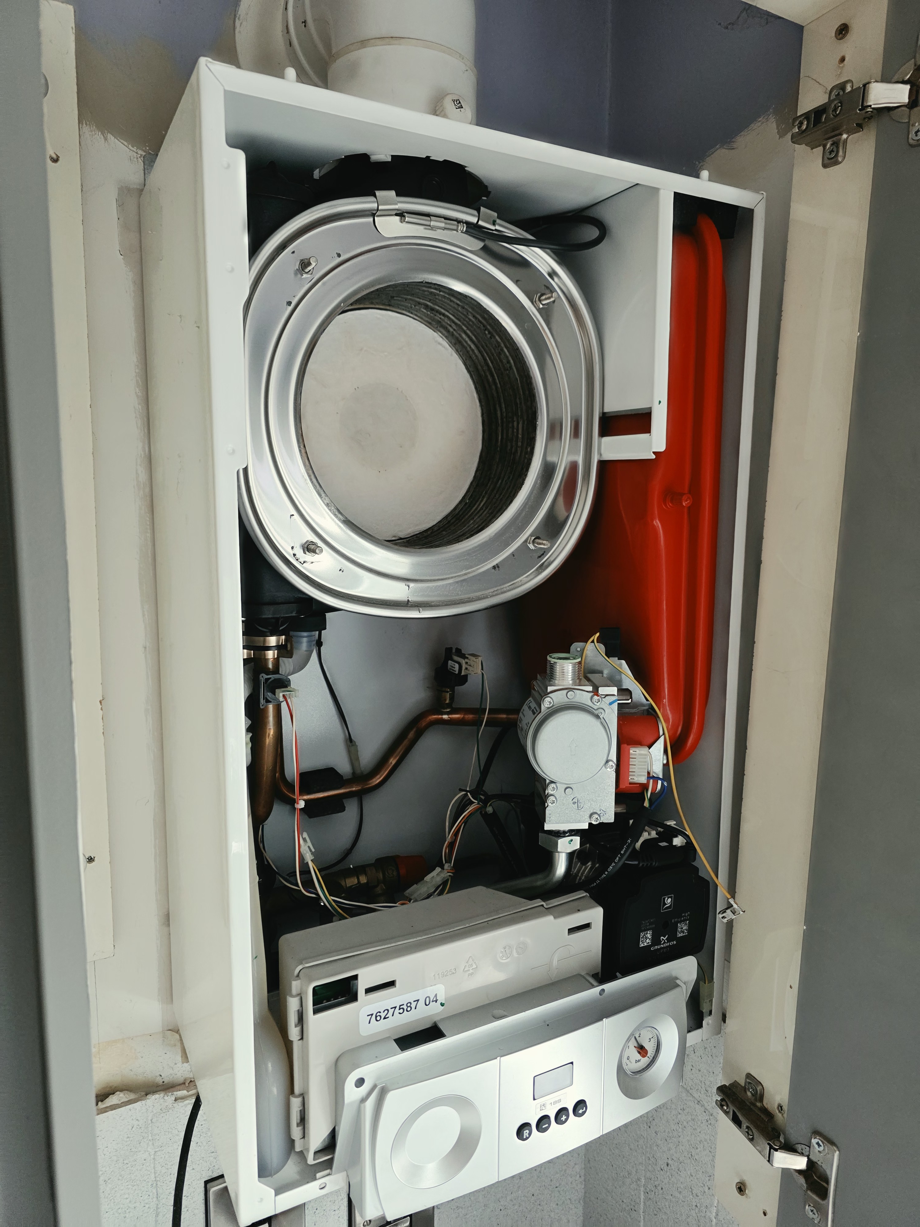 Opened Bosch gas boiler showing heat exchanger, gas valve, pump and wiring during a service